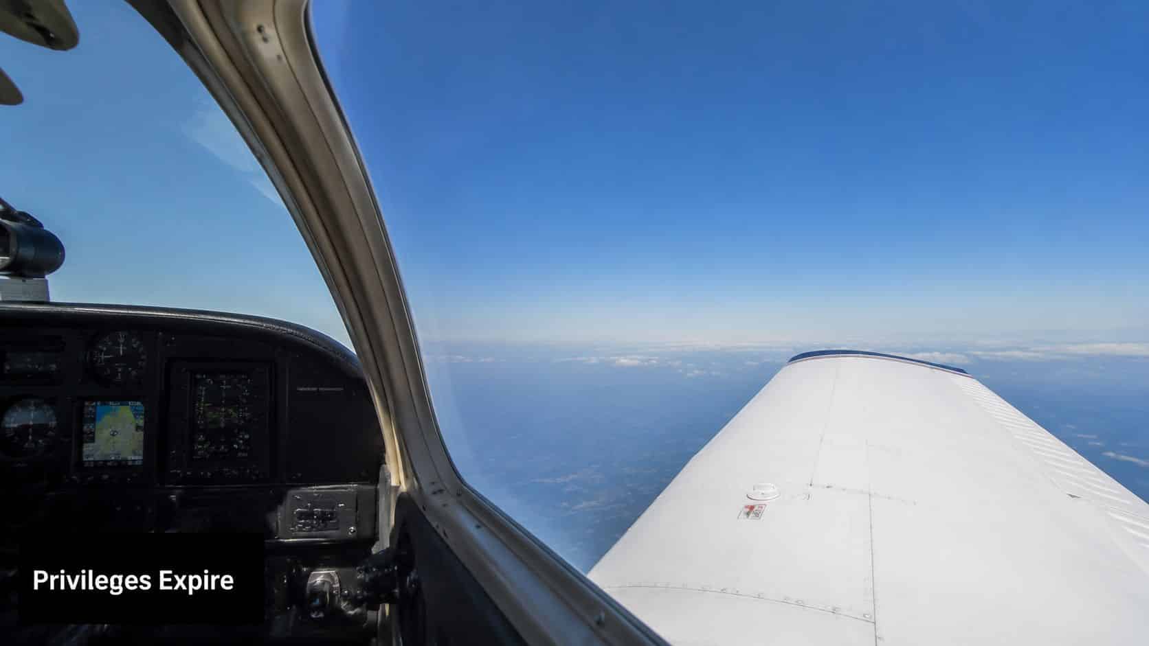 Private Pilot License Renewal: 2026 FAA Flight Review Guide 2 A view from the cockpit of a light aircraft flying high above clouds under a clear blue sky.