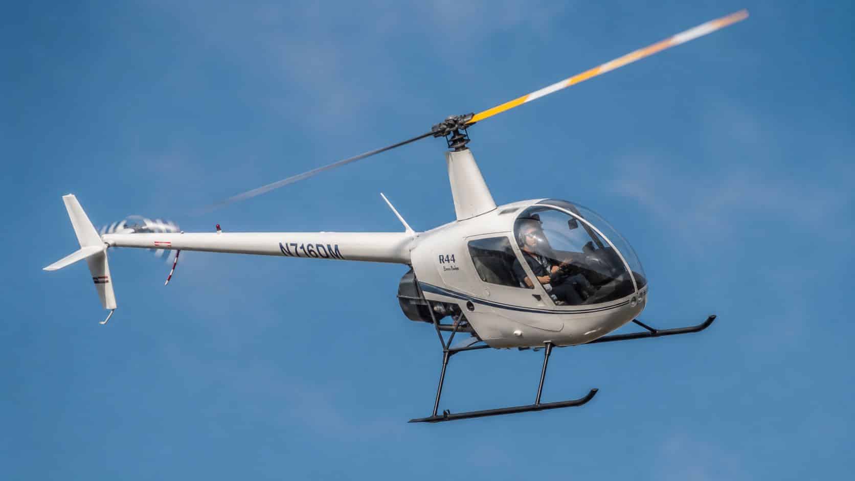 Robinson Helicopter Training: A Pilot's Complete Roadmap 3 A white Robinson R44 helicopter flying through a clear blue sky during a training flight.