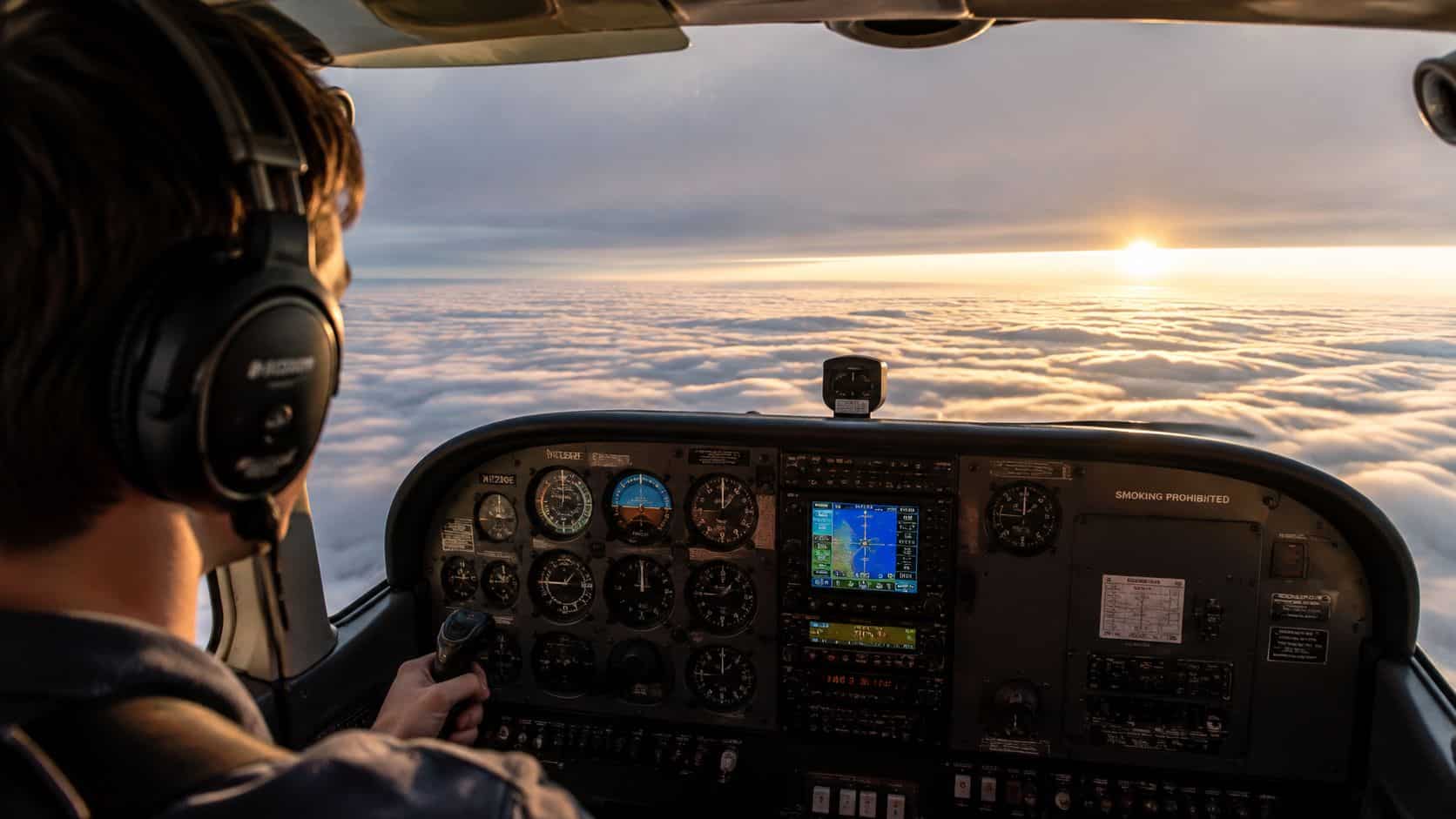 What Is an Instrument Rating and Why Pilots Earn One 2 A pilot wearing headphones sits in the cockpit of a small aircraft flying above a sea of clouds.
