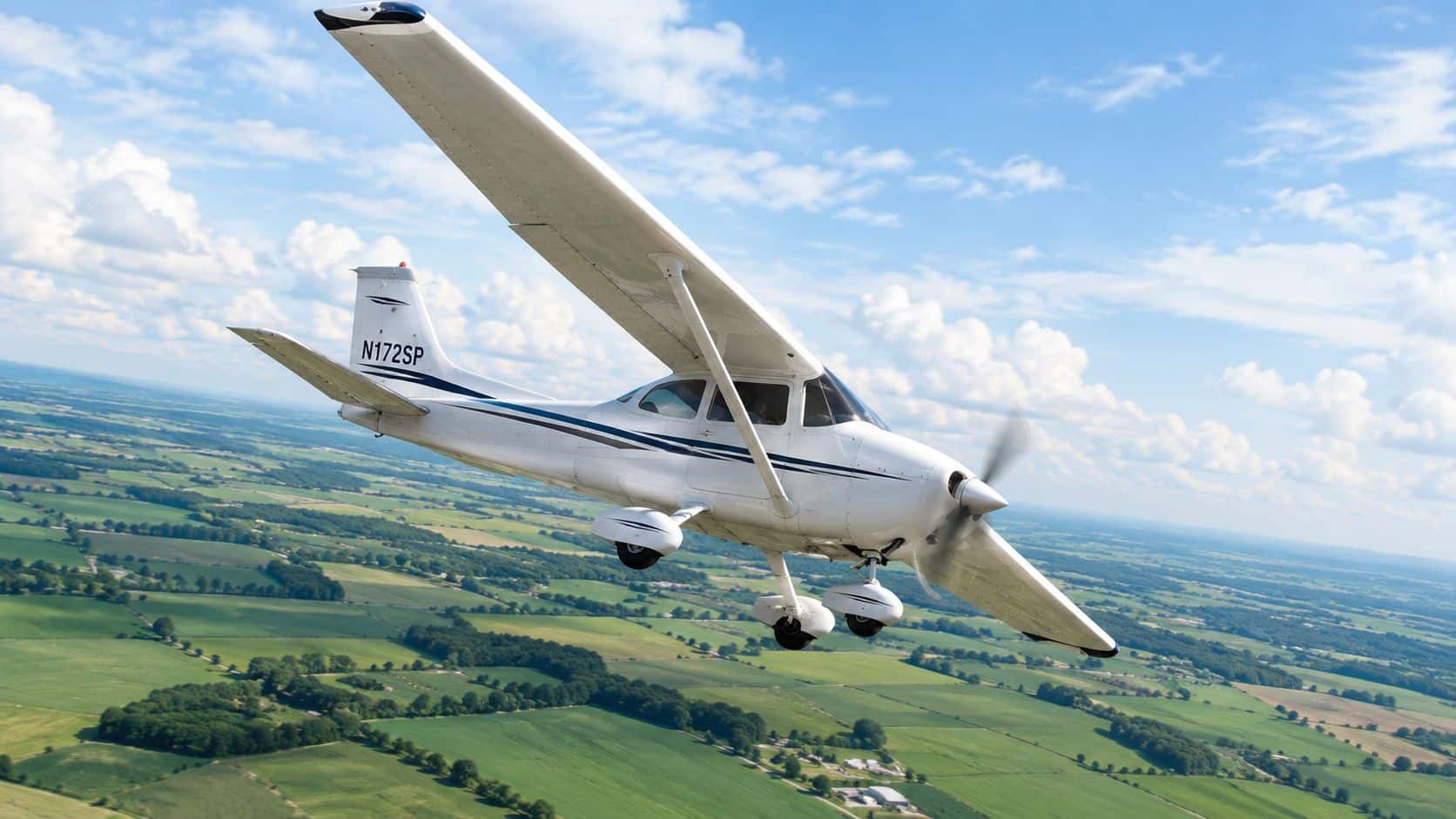 Private Pilot Checkride How to Pass the First Time 4 A small single-engine Cessna airplane flying over green agricultural fields on a sunny day.