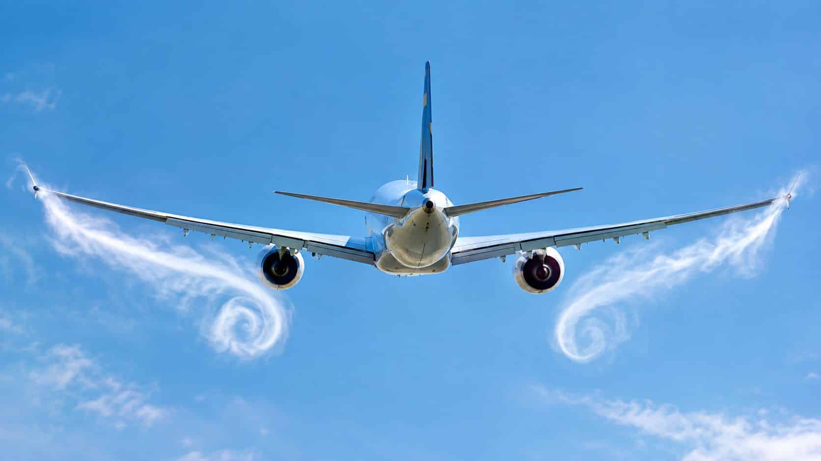 Wake Turbulence Avoidance: A Pilot's Practical Guide 2 A wide-body passenger airplane flying in a clear blue sky, showing visible wingtip vortices trail behind.
