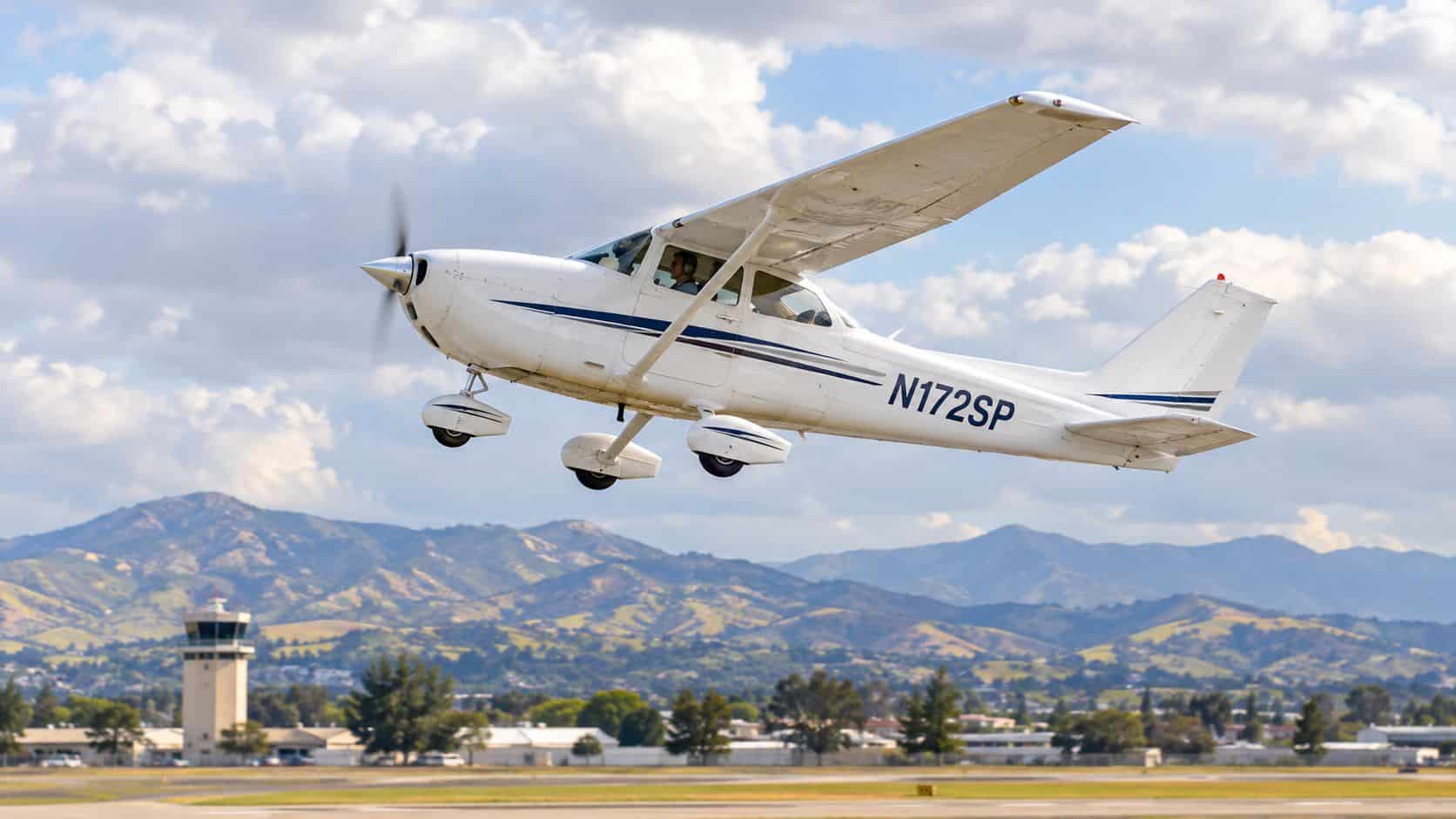 Aircraft Attitude Indicators Explained for Pilots 2 A white Cessna 172SP aircraft taking off from an airfield with a control tower and mountains behind.